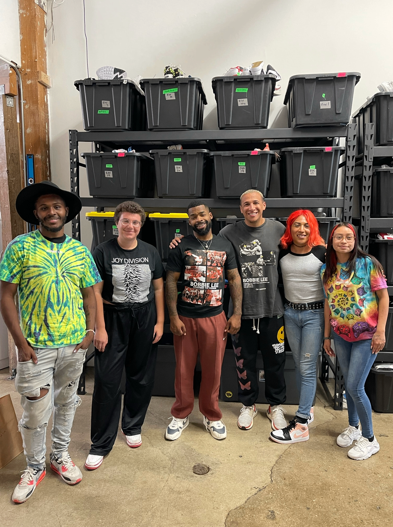Robins Garden founder Riley Robbins standing with five young community members in an organized supply space.